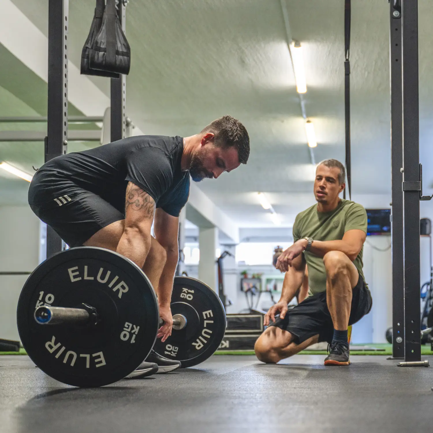 Osebni trener Dušan Cvetko med individualnim treningom v fitnesu vodi klienta k pravilni izvedbi mrtvega dviga (deadlift) z utežmi.